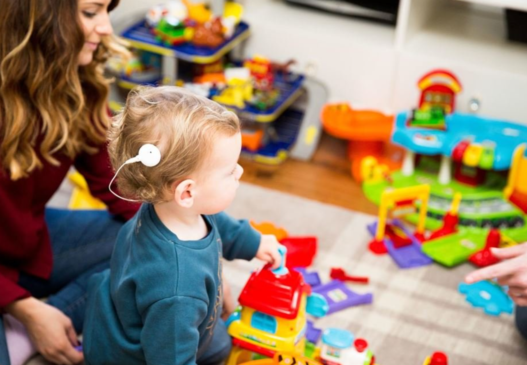 baby with cochlear implant plays with toys and parent